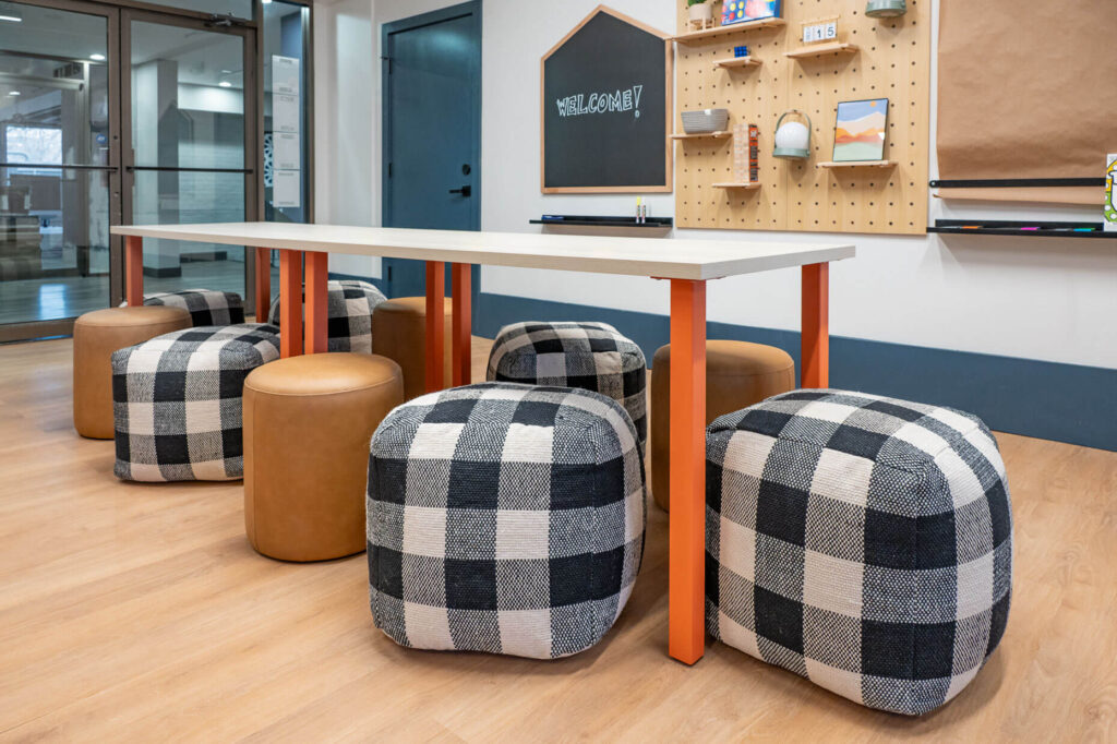 children's learning space with a dining table and ottoman seating around it with a chalkboard and peg board on the wall