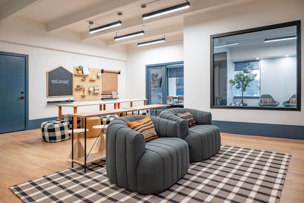 tables with dining chairs and plush seats across from television mounted on the wall and bookshelves adjacent to it with a view of office space through large windows