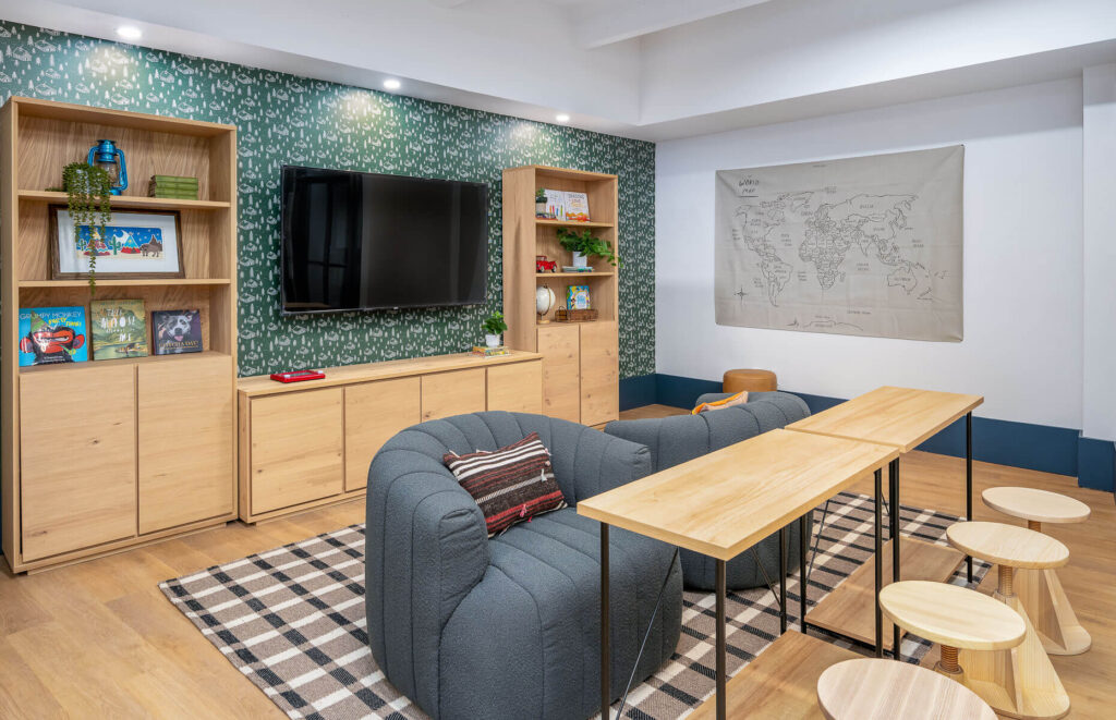 two tables with dining chairs and plush seats with television mounted on the wall and bookshelves adjacent to it