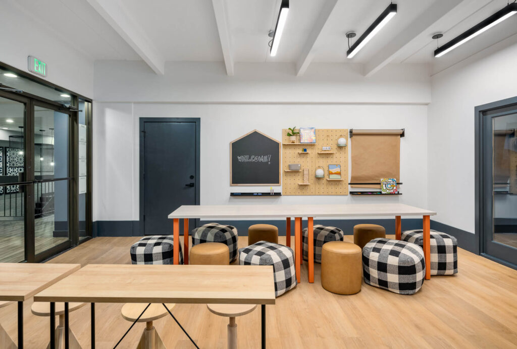 children's learning space with a dining table and ottoman seating around it with a chalkboard and peg board on the wall