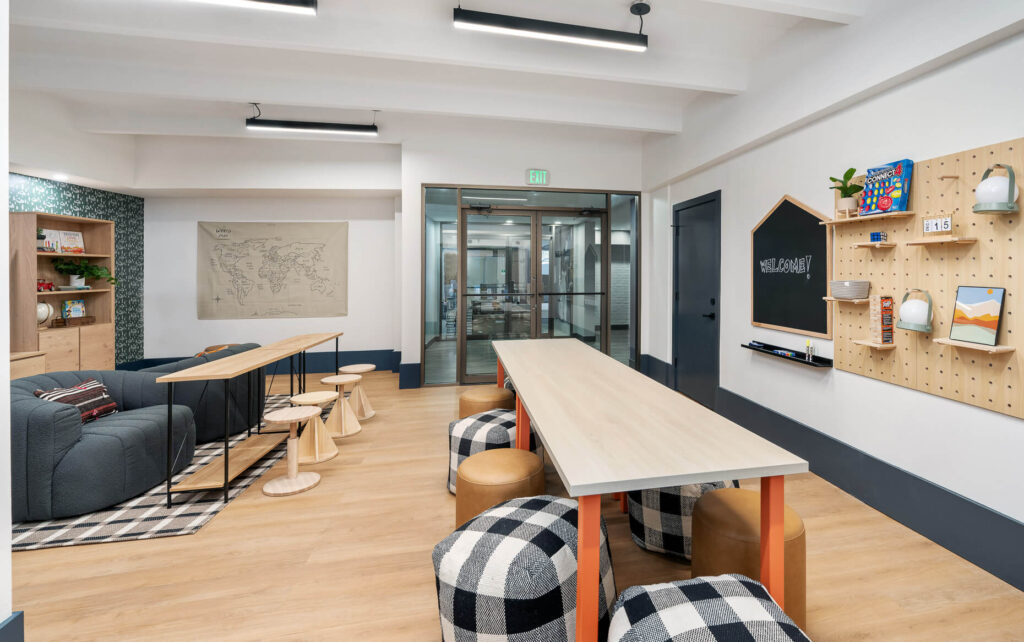 children's learning space with a dining table and ottoman seating around it with a chalkboard and peg board on the wall