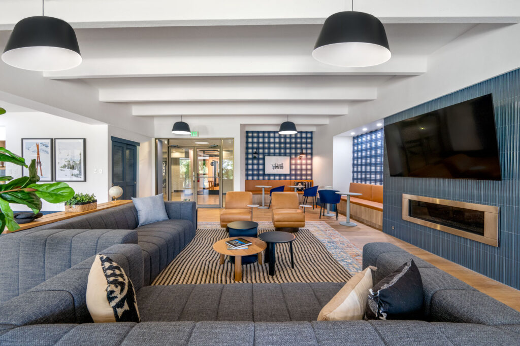 Elm at Panorama clubhouse entry seating space with sofas and armchair seating in a room with overhead and natural lighting with a television and fireplace