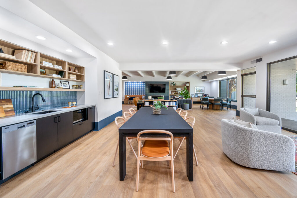 indoor community space with dining table and chairs next to kitchenette and seating space with television